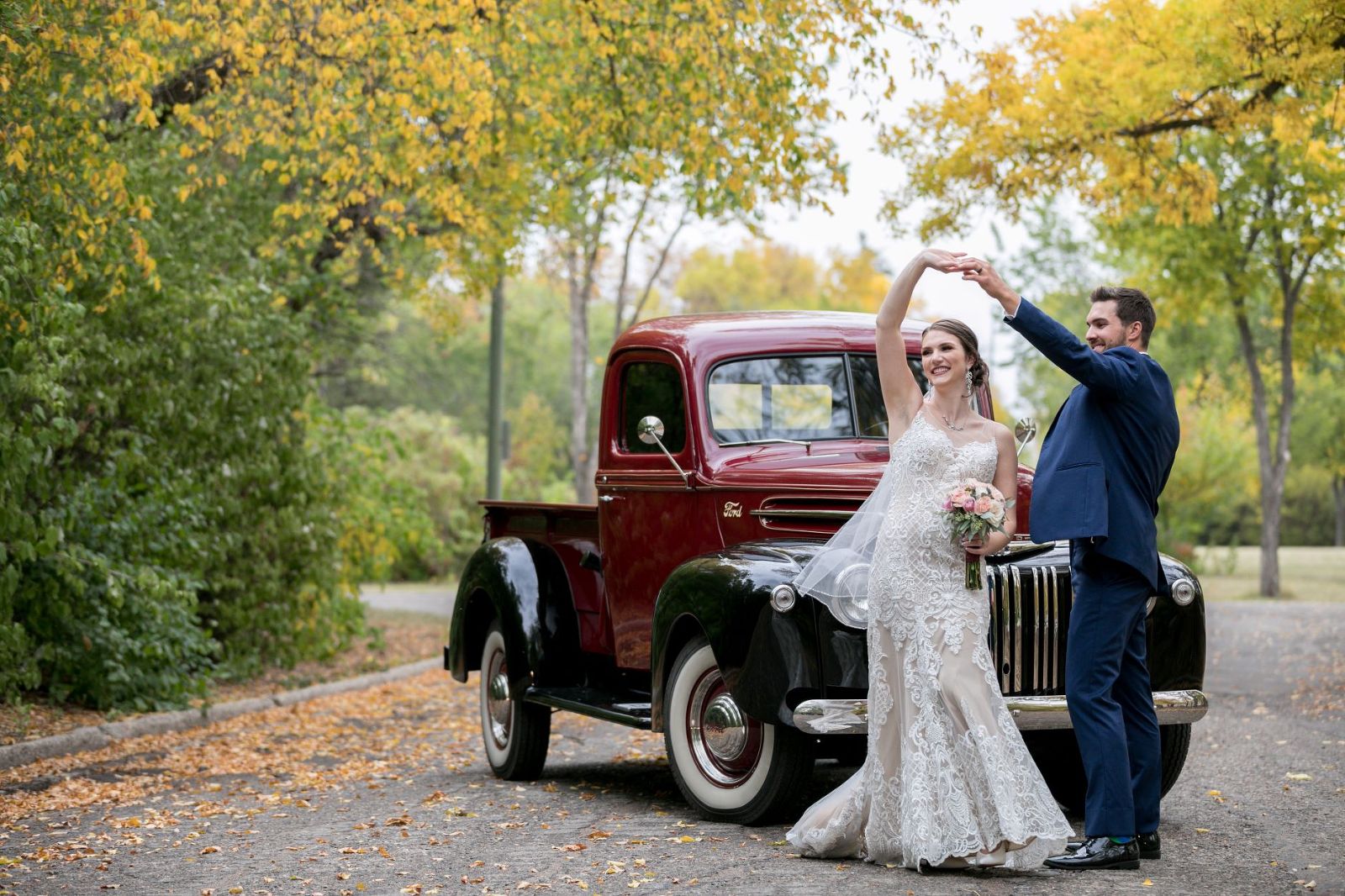 wedding photographed in Regina, Saskatchewan. A bride and groom dance in the road in front a classic truck with fall leaves.